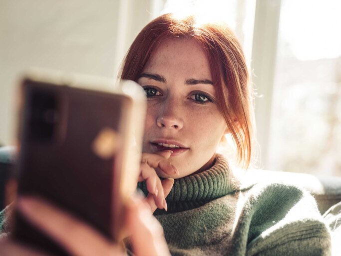 Rothaarige Frau schaut auf ihr Handy | © Getty Images/Guido Mieth