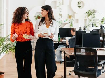 Zwei junge Frauen laufen durch ein modernes Büro | © Getty Images/Hinterhaus Productions