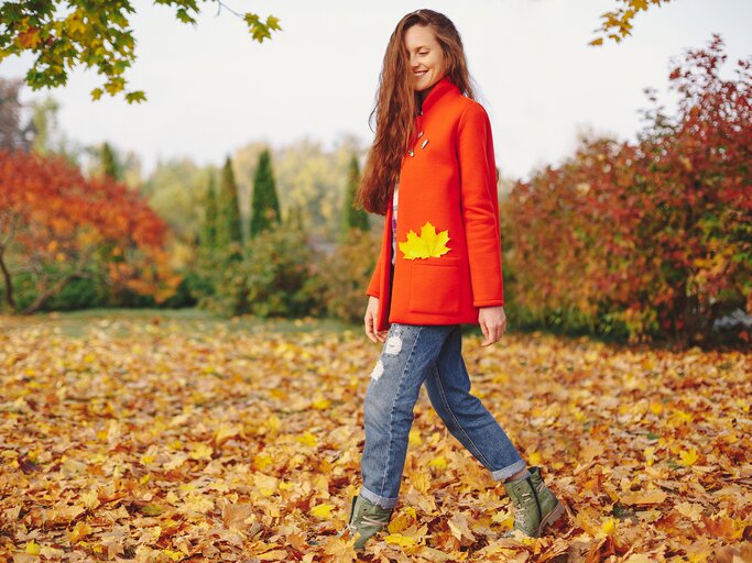 Eine Frau geht zwischen herbstlichen Blättern auf dem Boden | © GettyImages/ArthurHidden