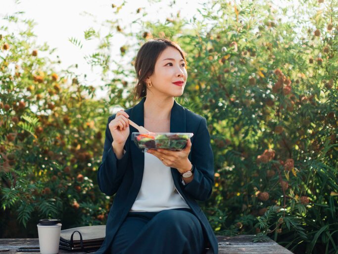 Business-Frau sitzt mit Salat auf einer Bank | © Getty Images/Oscar Wong