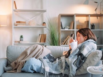Junge Frau sitzt frierend mit vielen Decken und Tee auf dem Sofa | © Adobe Stock/golubovy
