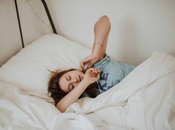 Frau liegt müde und verschlafen im Bett und reibt sich die Augen | © Unsplash/Kinga Howard 