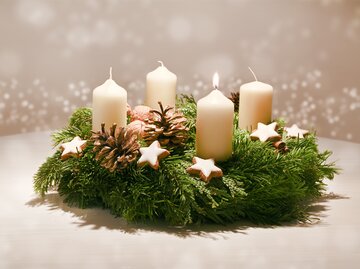 Erster Advent - geschmückter Adventskranz aus Tannenzweigen und immergrünen Zweigen mit weißen brennenden Kerzen | © Adobe Stock/Maren Winter