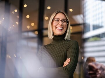 Eine junge Frau mit Brille lächelt und hinter ihr blitzen Lichter | © GettyImages/Westend61