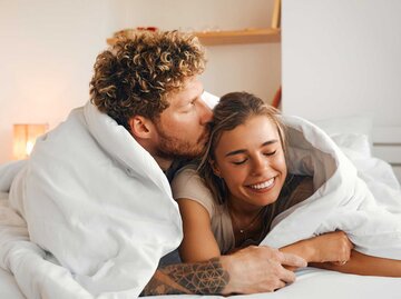 Mann gibt Partnerin einen Kuss. Sie liegen zusammen im Bett | © Adobe Stock/Valerii Apetroaiei