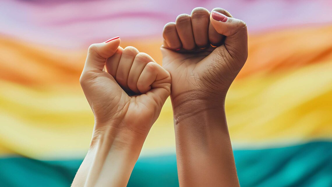 Zwei Fäuste vor einen Pride Flagge | © Adobe Stock/Jess rodriguez/KI