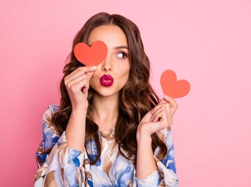 Frau hält zwei Schablonen in Herzform in der Hand und macht einen Kussmund | © Adobe Stock/deagreez