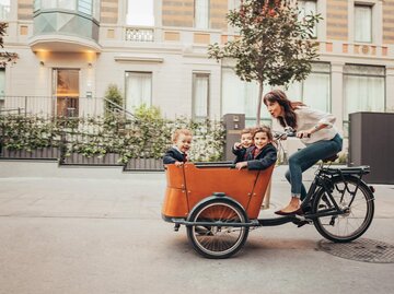 Frau fährt mit drei Kindern im Anhänger Rad | © Getty Images/Orbon Alija