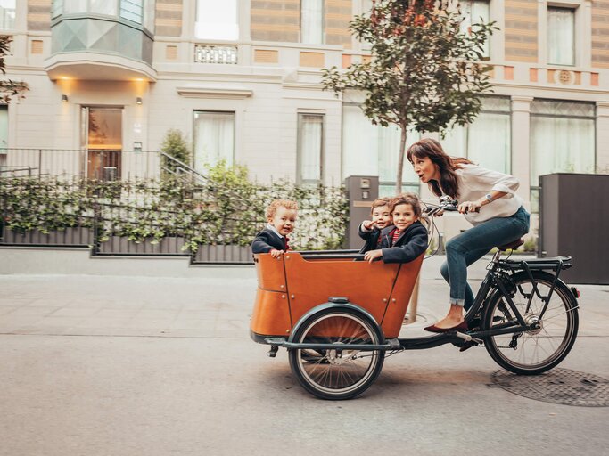 Frau fährt mit drei Kindern im Anhänger Rad | © Getty Images/Orbon Alija