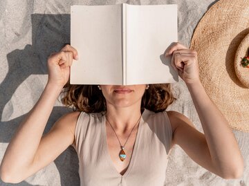 Frau hält Buch über dem Gesicht | © Getty Images/Carlos Pintau