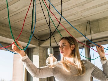 Frau werkelt an Deckenlampe  | © Getty Images/Westend61