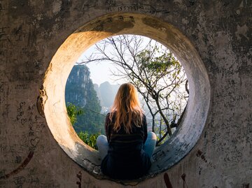 Frau sitzt vor runder Öffnung und schaut in die Ferne | © Getty Images/Andrii Lutsyk/ Ascent Xmedia