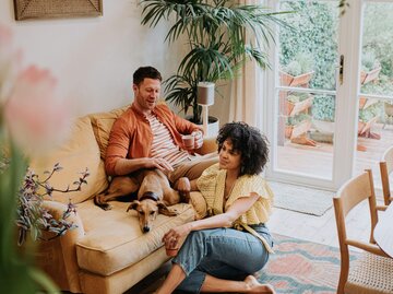 Mann, Frau und Hund sitzen im Wohnzimmer | © Getty Images/Catherine Falls Commercial