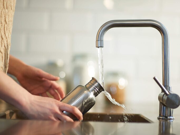 Frau reinigt Trinkflasche mit Wasser | © Getty Images/Dougal Waters