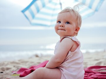 Kleines Kind sitzt am Strand und schaut in die Kamera | © Getty Images/Guido Mieth