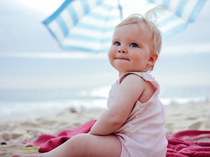 Kleines Kind sitzt am Strand und schaut in die Kamera | © Getty Images/Guido Mieth