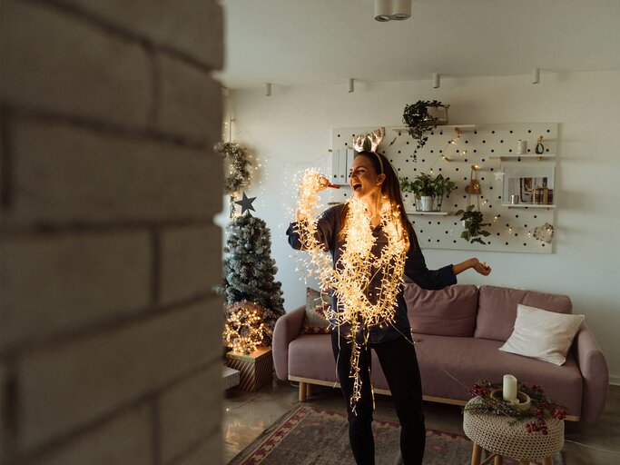 Frau hat Lichterkette für Weihnachtsbaum um und singt | © Getty Images/AleksandarNakic