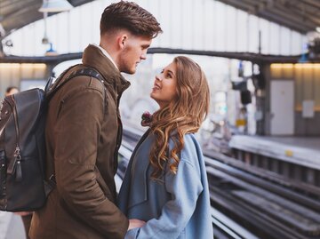 Junges Paar steht an einem Bahnsteig und schaut sich verliebt an | © Getty Images/anyaberkut