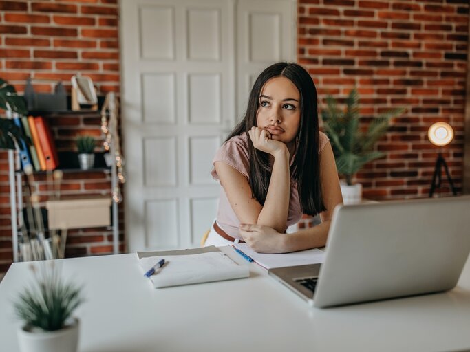 Junge Frau sitzt im Büro am Schreibtisch und denkt nach | © Getty Images/supersizer