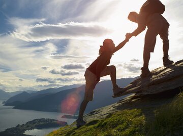 Mann hilft Frau dabei, einen Berg hochzulaufen | © Getty Images/Jacobs Stock Photography Ltd