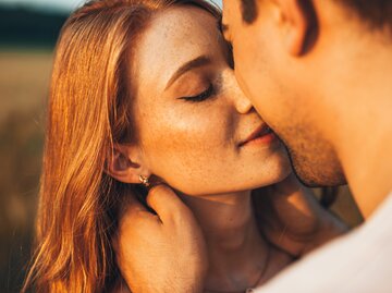 Nahaufnahme eines sommersprossigen Mädchens, das ihren Freund küsst, während sie auf einem Outdoor-Date sind. | © Getty Images/Strelciuc Dumitru