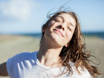Junge Frau hält glücklich die Arme in die Luft und hat die Augen geschlossen | © Getty Images/Letizia McCall