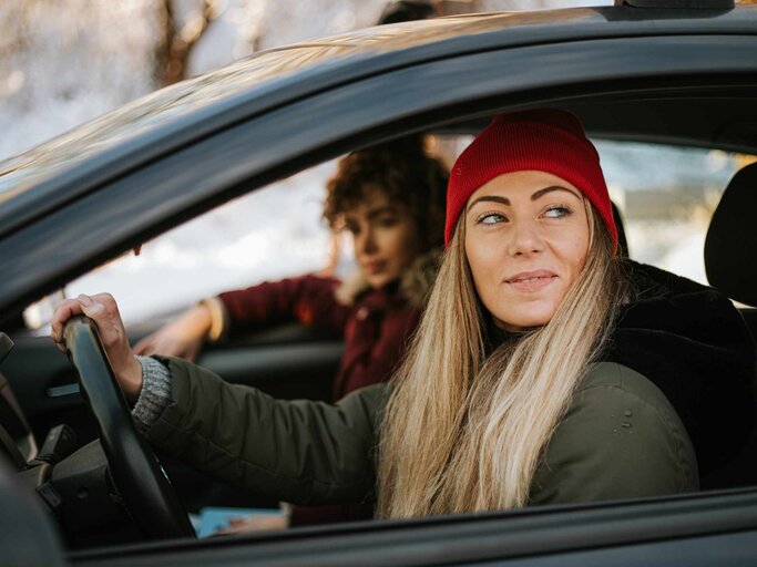 Junge Frau sitzt hinter dem Steuer eines Autos und schaut aus dem Fenster | © Getty Images/Andrija Nikolic