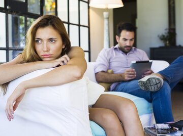 Frau sitzt frustriert auf der Couch während ihr Partner auf sein Tablet schaut | © Getty Images/PhotoAlto/Frederic Cirou