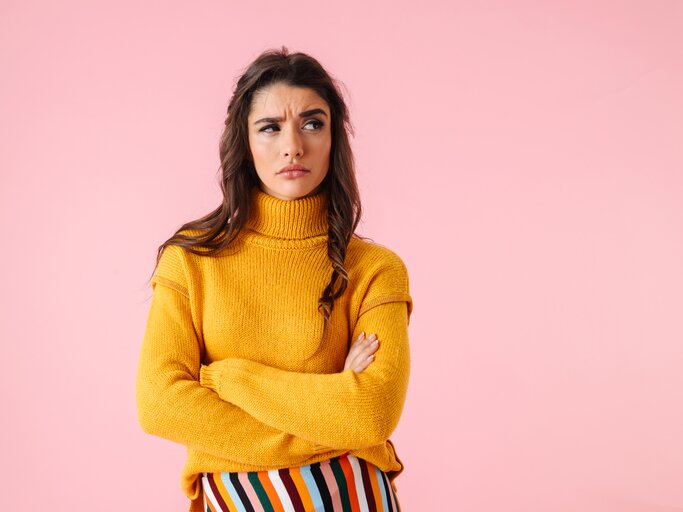 Frau mit skeptischem Gesichtsausdruck trägt gelben Pullover, bunte Hose und verschränkt die Arme  | © Getty Images/DeanDrobot