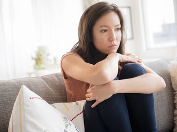 Junge Frau sitzt nachdenklich auf der Couch | © Getty Images/JGI/Jamie Grill