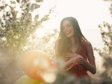Junge Frau lächelt und hält Ballons fest | © Getty Images/SrdjanPav