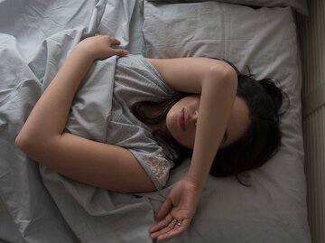 Frau liegt im Bett, hat den Arm über dem Gesicht und kann nicht schlafen. | © Getty Images / Tetra Images