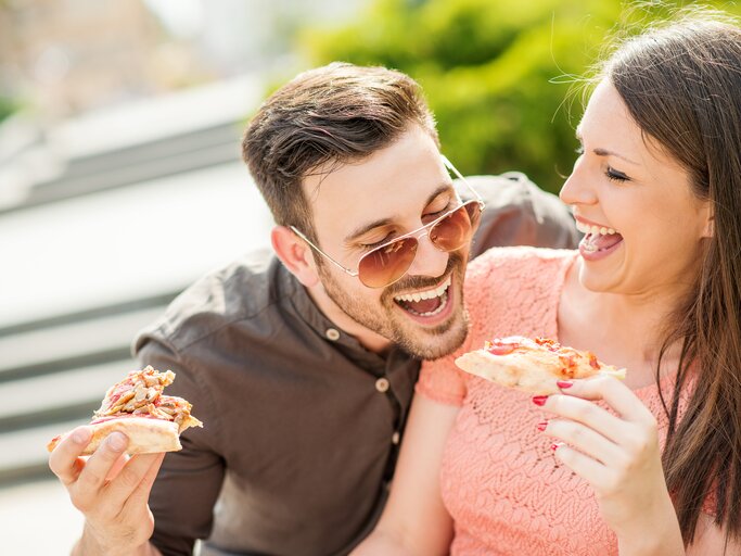 Mann und Frau essen Pizza. Mann versucht dabei Stück von der Pizza der Frau abzubeißen | © Getty Images/Ivanko_Brnjakovic