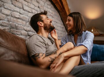 Paar sitzt zusammen auf der Couch, Frau sitzt dabei auf dem Schoß vom Mann | © Getty Images/bernardbodo