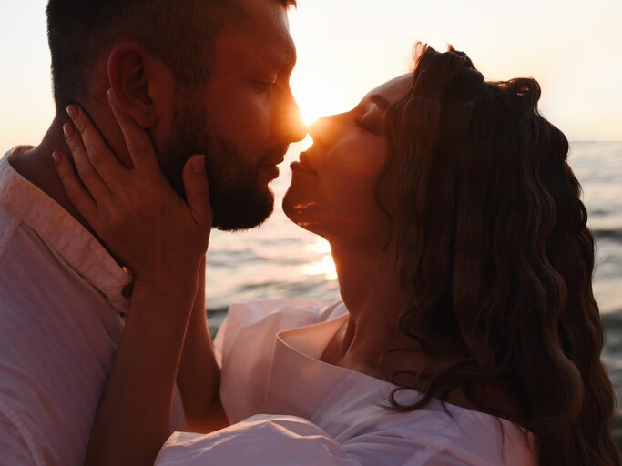Mann und Frau küssen sich bei Sonnenuntergang | © Getty Images/MarynaTerletska