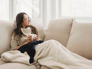 Frau liegt gemütlich auf der Couch und entspannt sich | © GettyImages/Vasil Dimitrov
