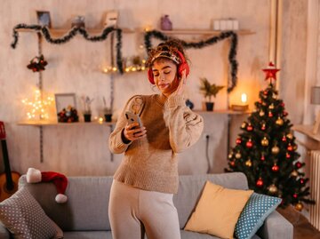 Frau mit Kopfhörern in weihnachtlich geschmücktem Wohnzimmer | © Getty Images/urbazon
