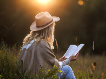 Frau ließt ein Buch draußen auf dem Feld | © Getty Images/Zbynek Pospisil