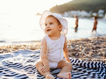 Baby-Mädchen mit Hut sitzt auf Handtuch am Strand im Sommer | © Getty Images/Drazen_