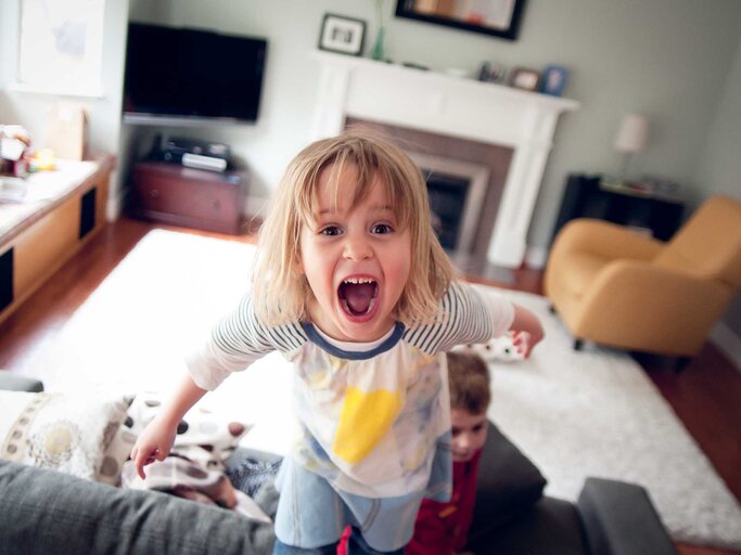 Junges Mädchen steht im Wohnzimmer auf der Couch und schreit in die Kamera. | © Getty Images / Teresa Short