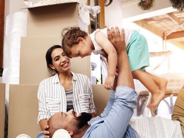 Fröhliches, junges Paar spielt mit Kind zwischen Umzugskartons | © Getty Images/Dean Mitchell