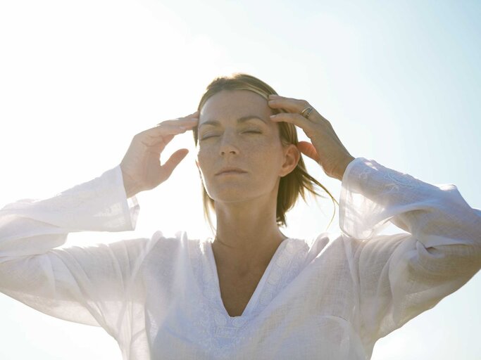 Frau mit weißer Bluse hält beide Hände an ihren Kopf.  | © Getty Images / ZenShui/Alix Minde