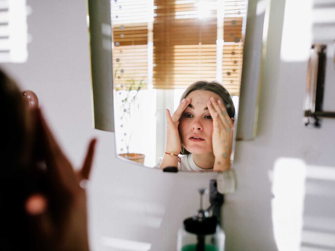 Frau steht vor dem Spiegel und betrachtet ihr Gesicht. | © Getty Images / Willie B. Thomas