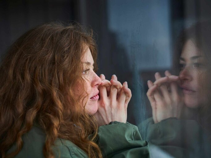 Frau mit roten Haaren schaut grübelnd aus dem Fenster | © Getty Images/Justin Case