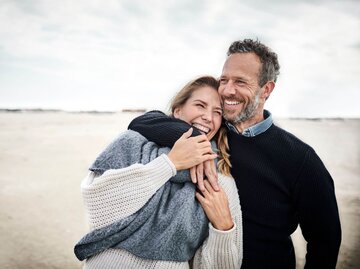 Mann umarmt Frau am Strand | © Getty Images/Oliver Rossi