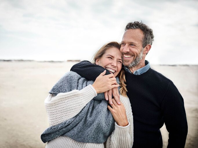 Mann umarmt Frau am Strand | © Getty Images/Oliver Rossi