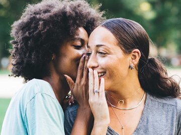 Zwei Frauen stehen nebeneinander und lästern hinter vorgehaltenen Händen. | © Getty Images / Westend61