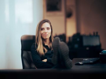 Junge Frau sitzt auf einem Bürostuhl und hat die Füße auf dem Tisch. | © Getty Images / nicoletaionescu