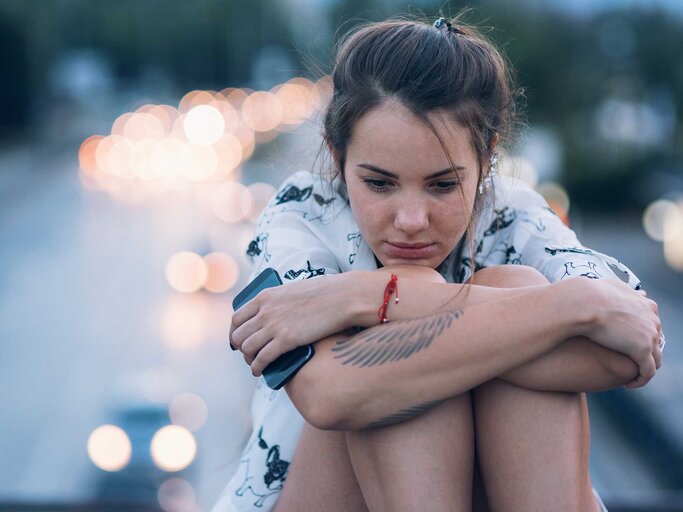 Frau sitzt mit angezogenen Beinen auf der Straße und hat ist traurig. | © Getty Images / Mixmike