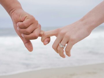 Paar hält am Wasser Händchen und die Frau trägt einen Verlobungsring. | © Getty Images / REB Images
